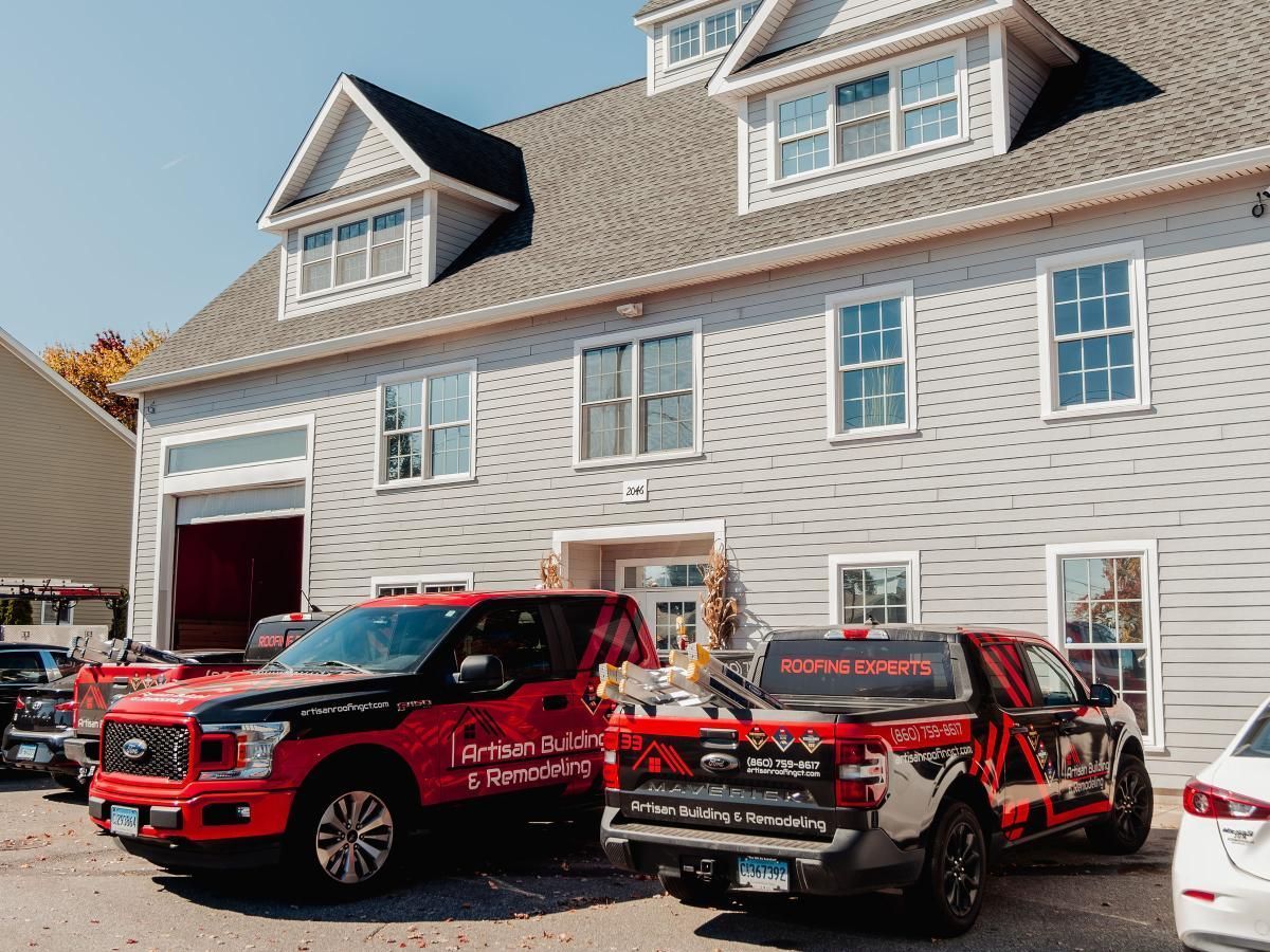 Two red trucks are parked in front of a large white house.