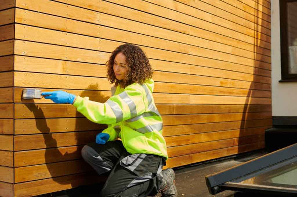 A woman is painting a wooden wall with a brush.