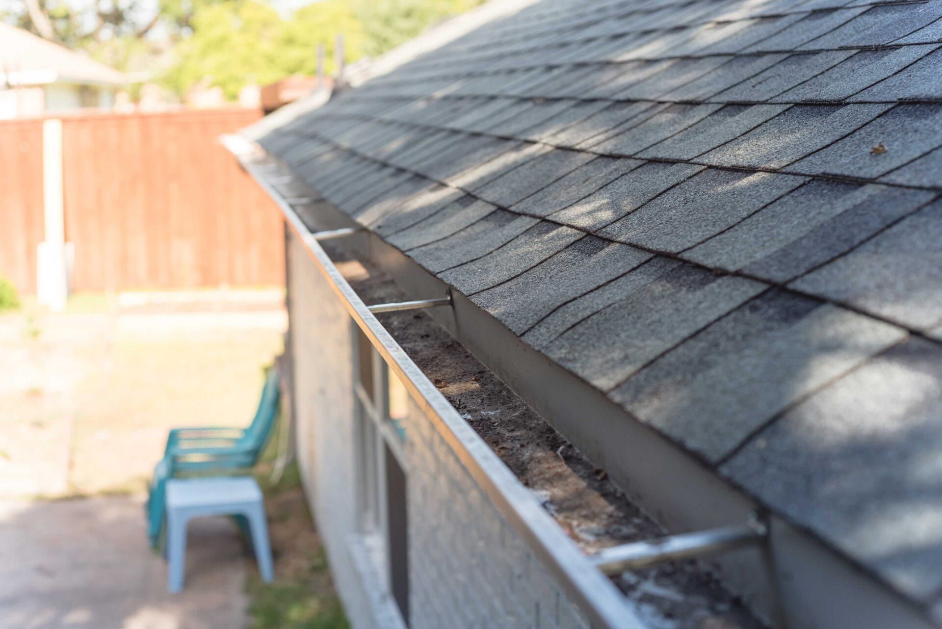 A gutter on the side of a house with a roof in the background.