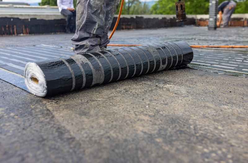 A person is rolling a roll of waterproofing material on a roof.