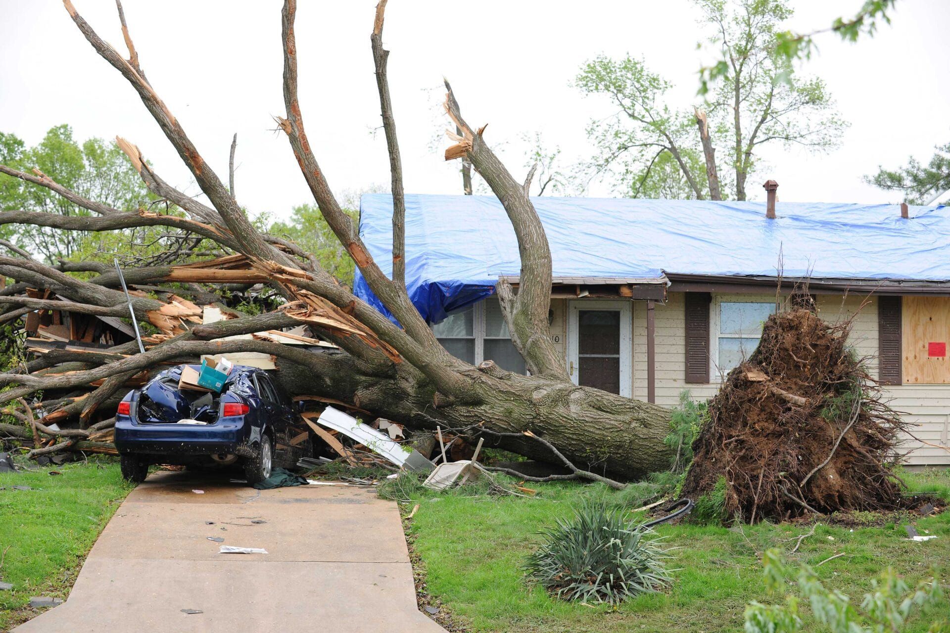 A car is parked in front of a house that has been damaged by a tornado.