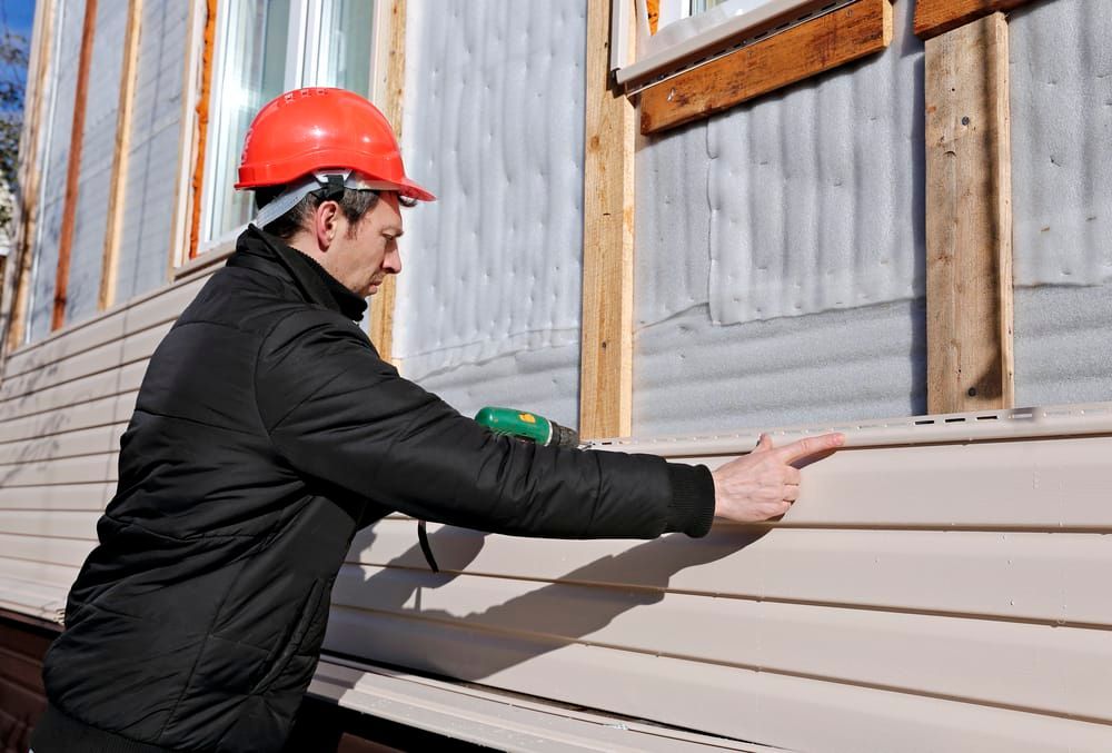 A man wearing a hard hat is installing siding on the side of a building.