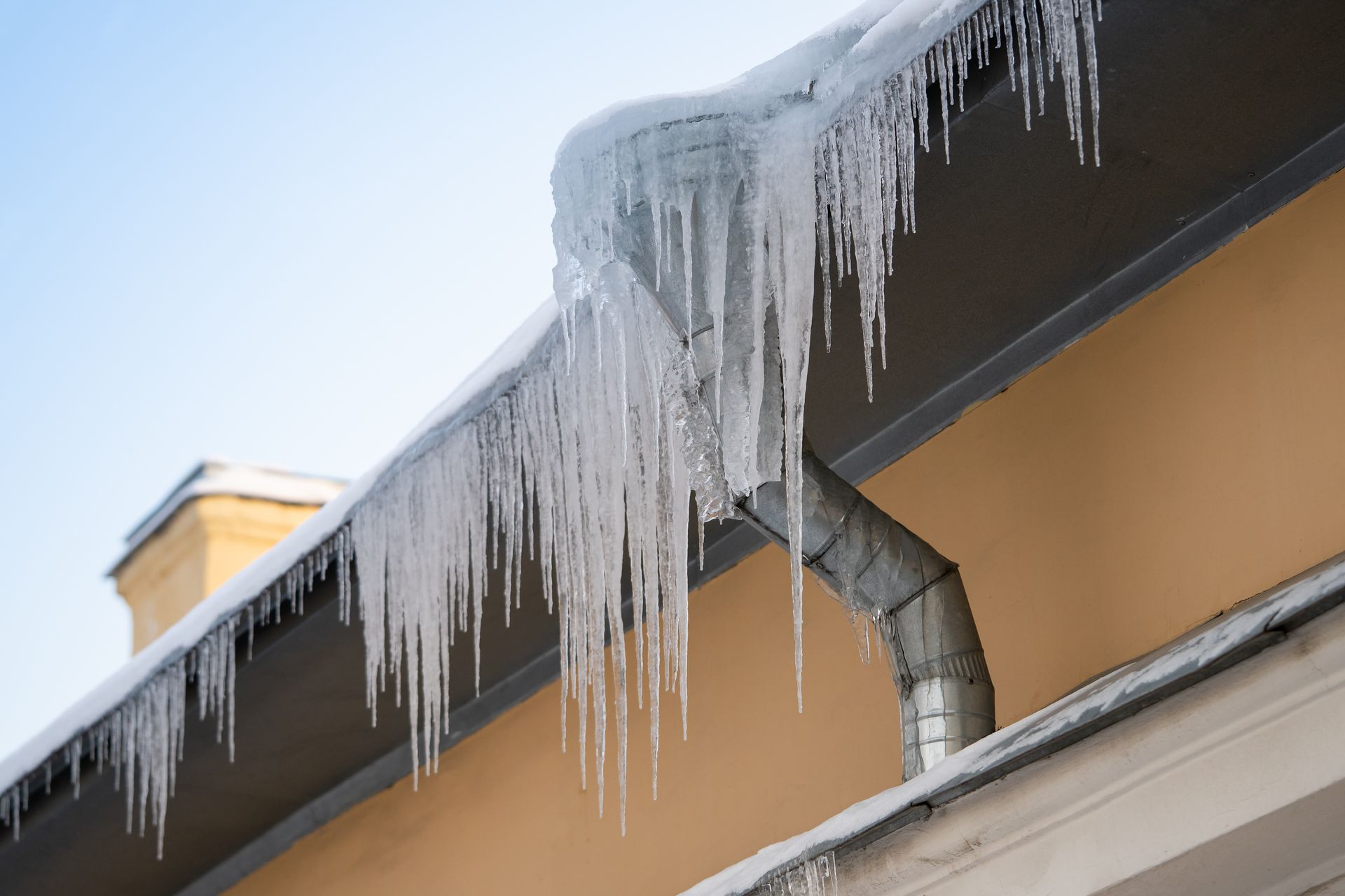 Icicles hanging from a gutter on a building with a beige exterior, blue sky background.