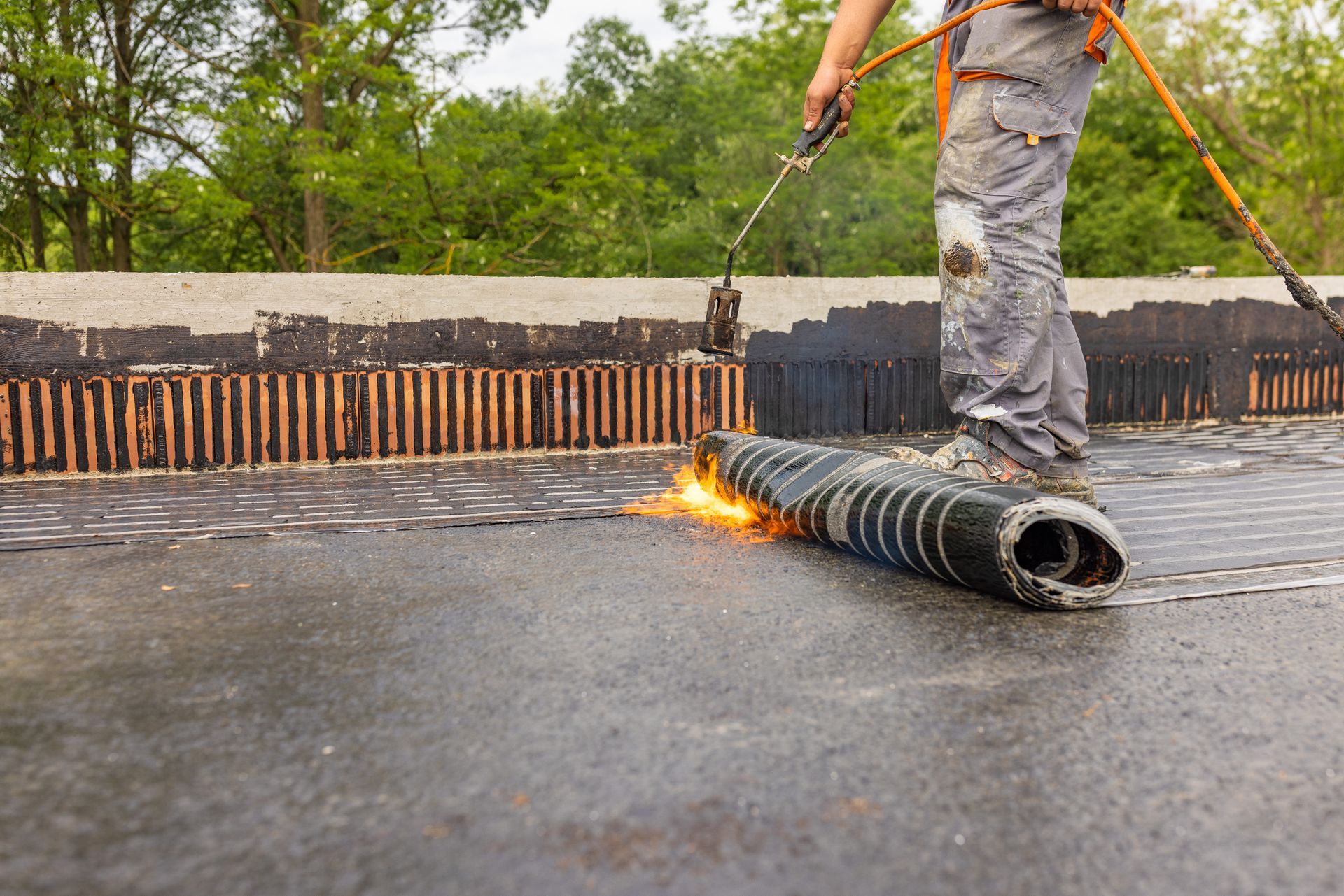 A man is using a torch to apply waterproofing to a roof.