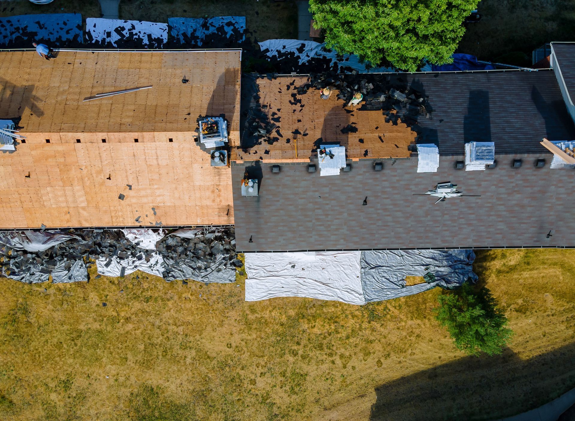 Aerial view of two adjacent house rooftops, one tan and one gray, beside trees and a grassy yard.