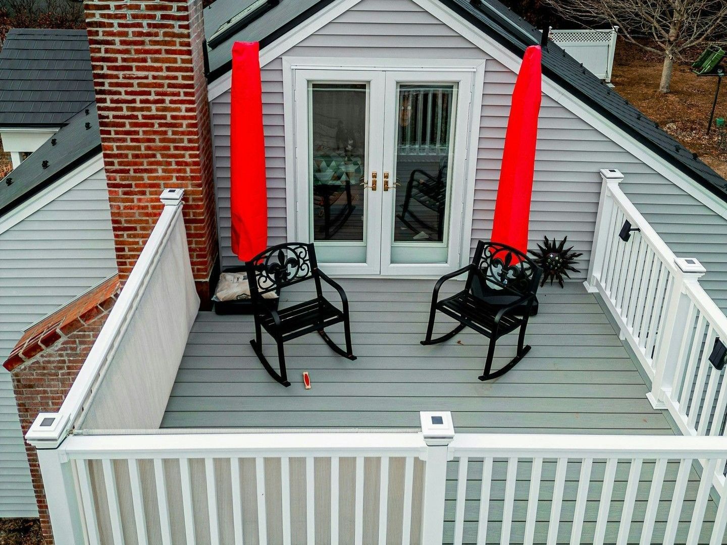 There are two rocking chairs on the deck of a house.