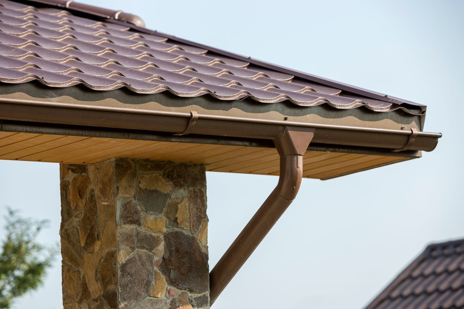 Stone house pillar supporting a brown tiled roof and copper gutter against a blue sky