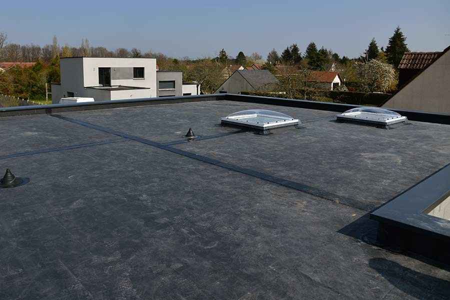 A roof with a few skylights on it and a house in the background.