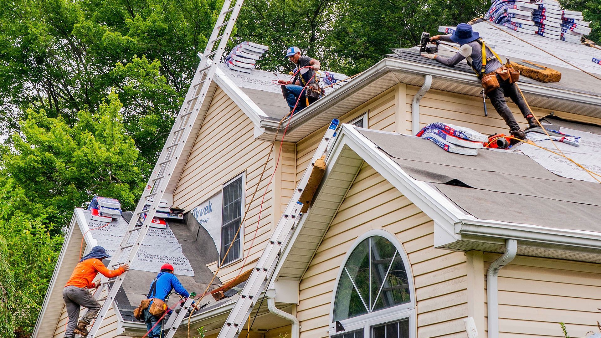 Roofers installing new shingles on a residential house; workers wearing safety gear and using tools.