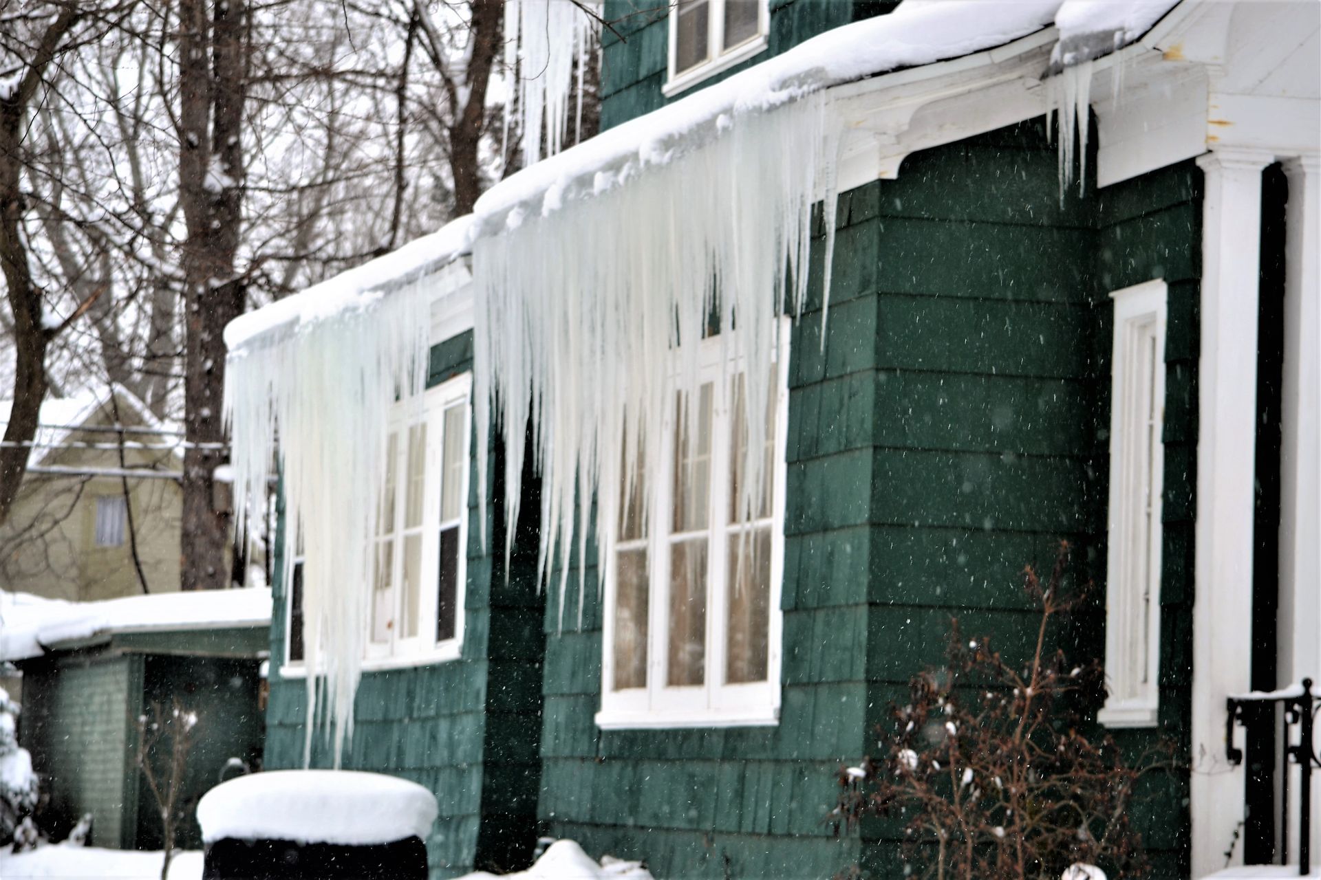 Green house with large icicles hanging from the roof in a snowy setting.