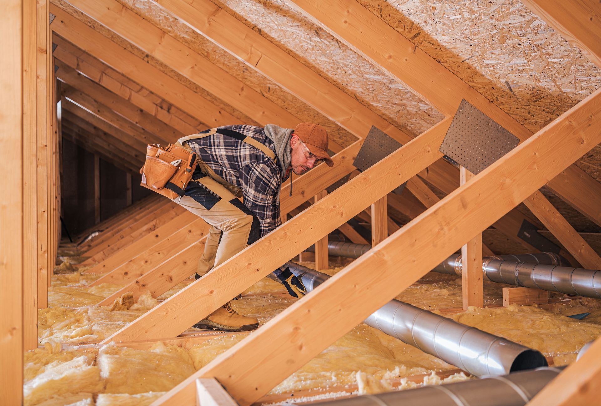 Person inspecting a wooden attic with insulation, ductwork, and beams.