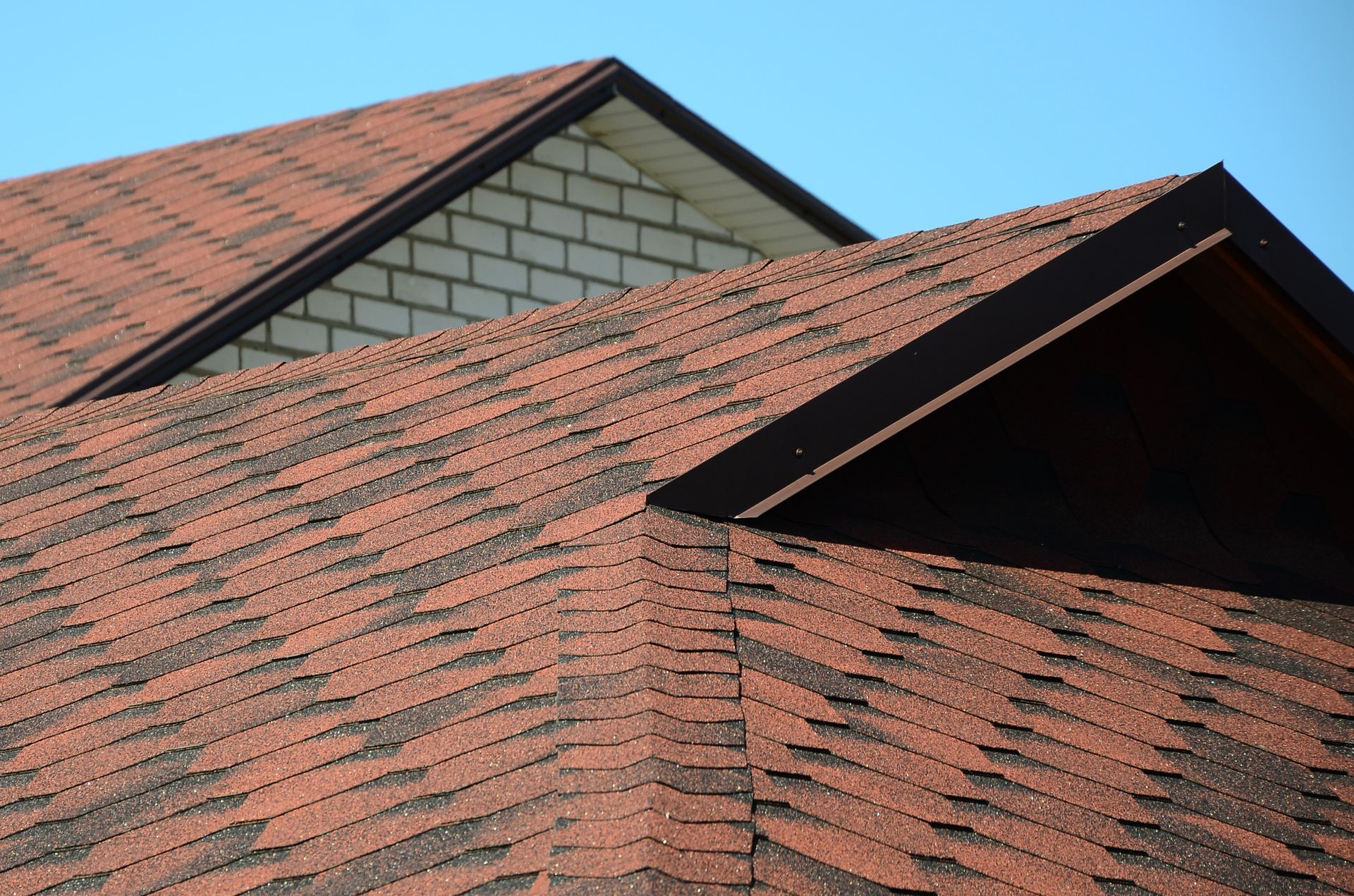 Close-up of red shingle rooftops with triangular dormers against a blue sky