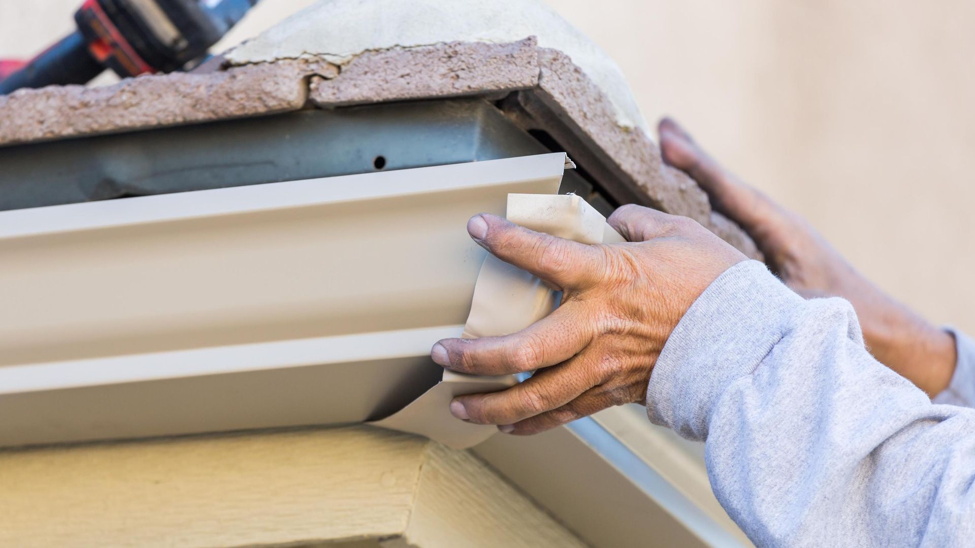 A man is installing a gutter on the side of a house.