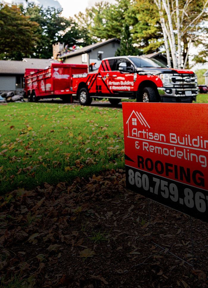 A red truck is parked next to a sign that says artisan builder & remodeling roofing