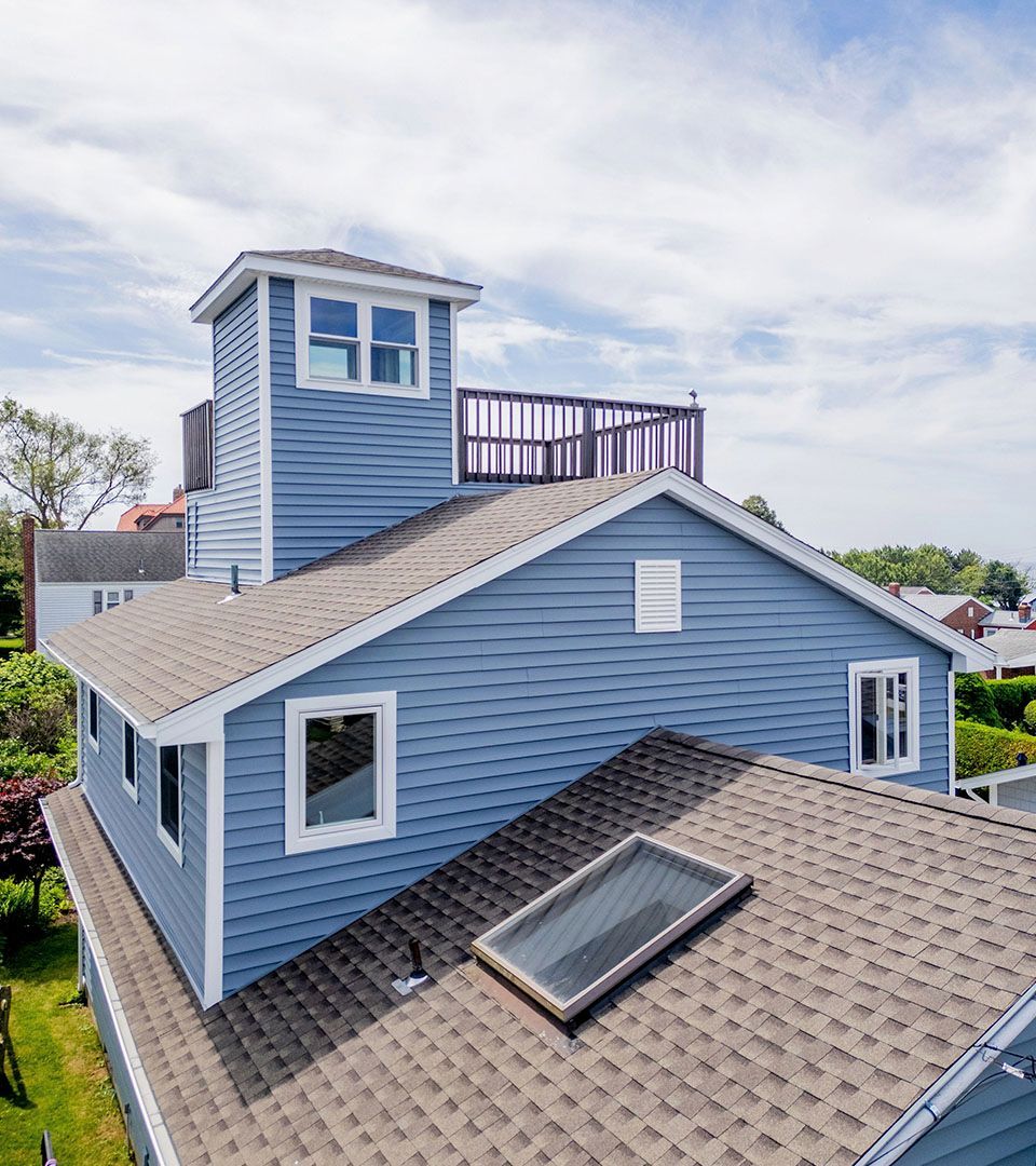 Blue house with a rooftop deck and a tower; cloudy sky.