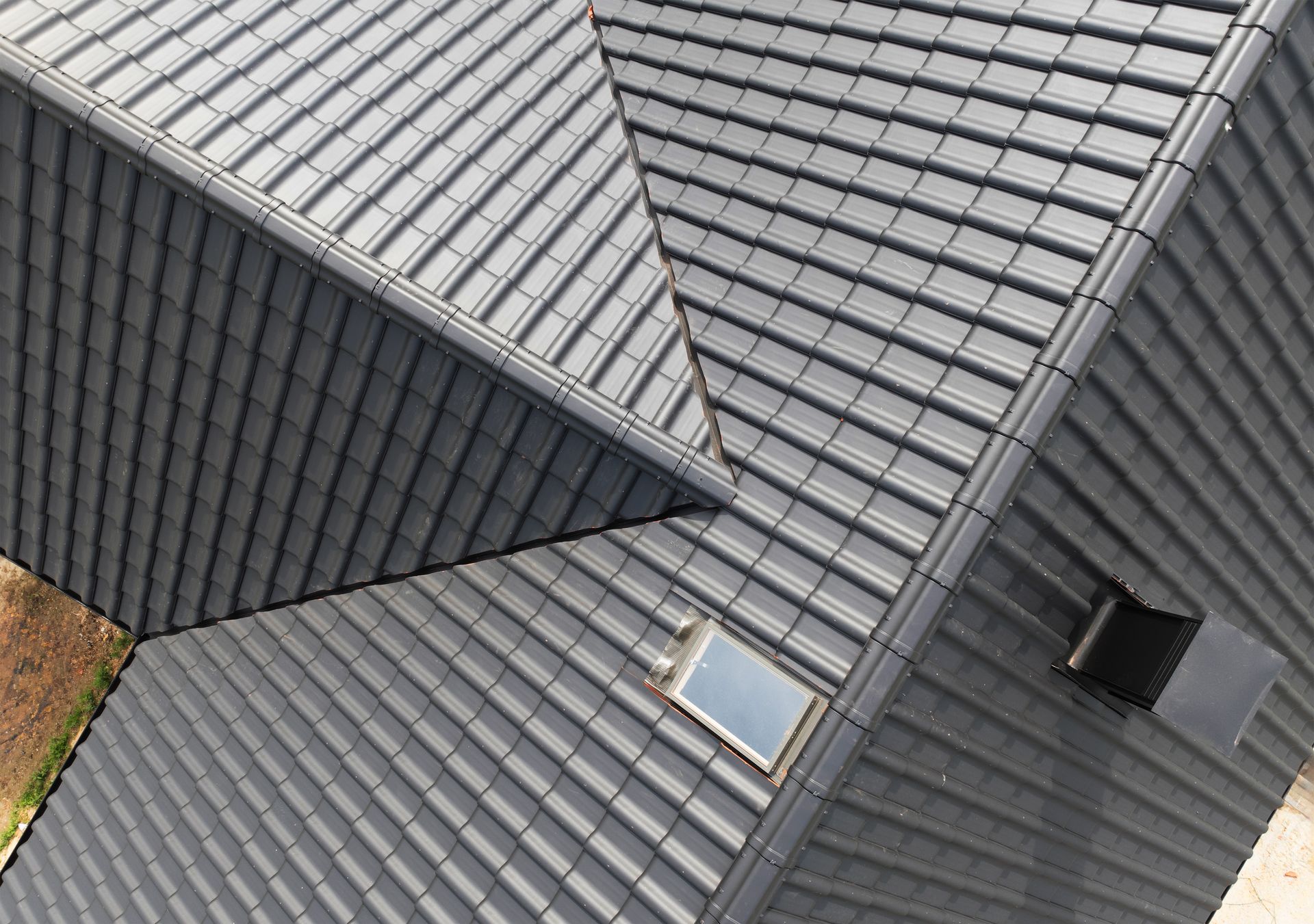 Aerial view of intersecting gray metal roofs with skylights and a chimney.
