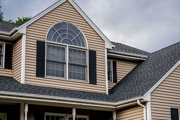 The roof of a house with a large window and black shutters.