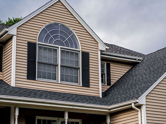 The roof of a house with a large window and black shutters.