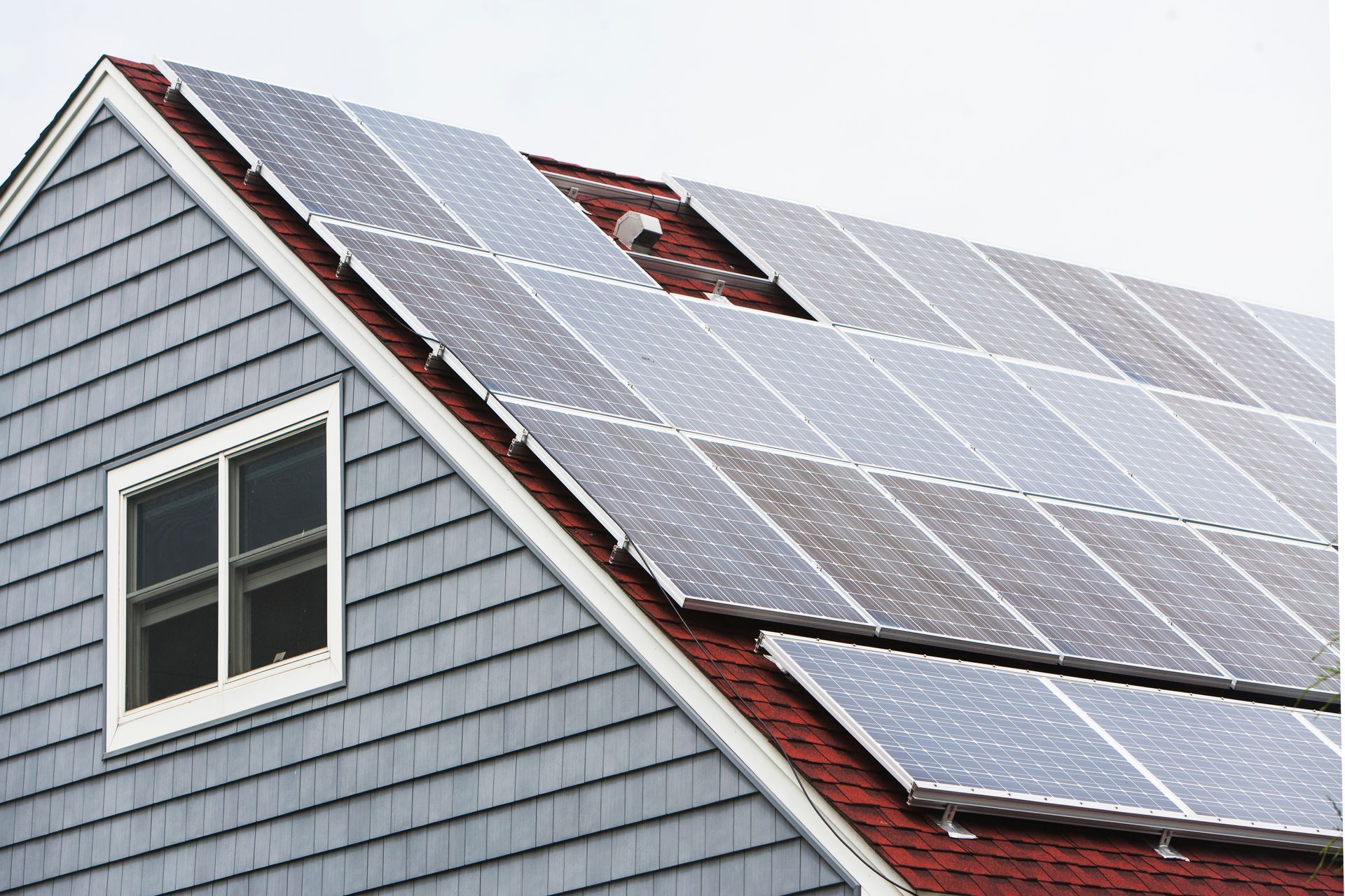 Solar panels installed on a house roof above a white-framed window
