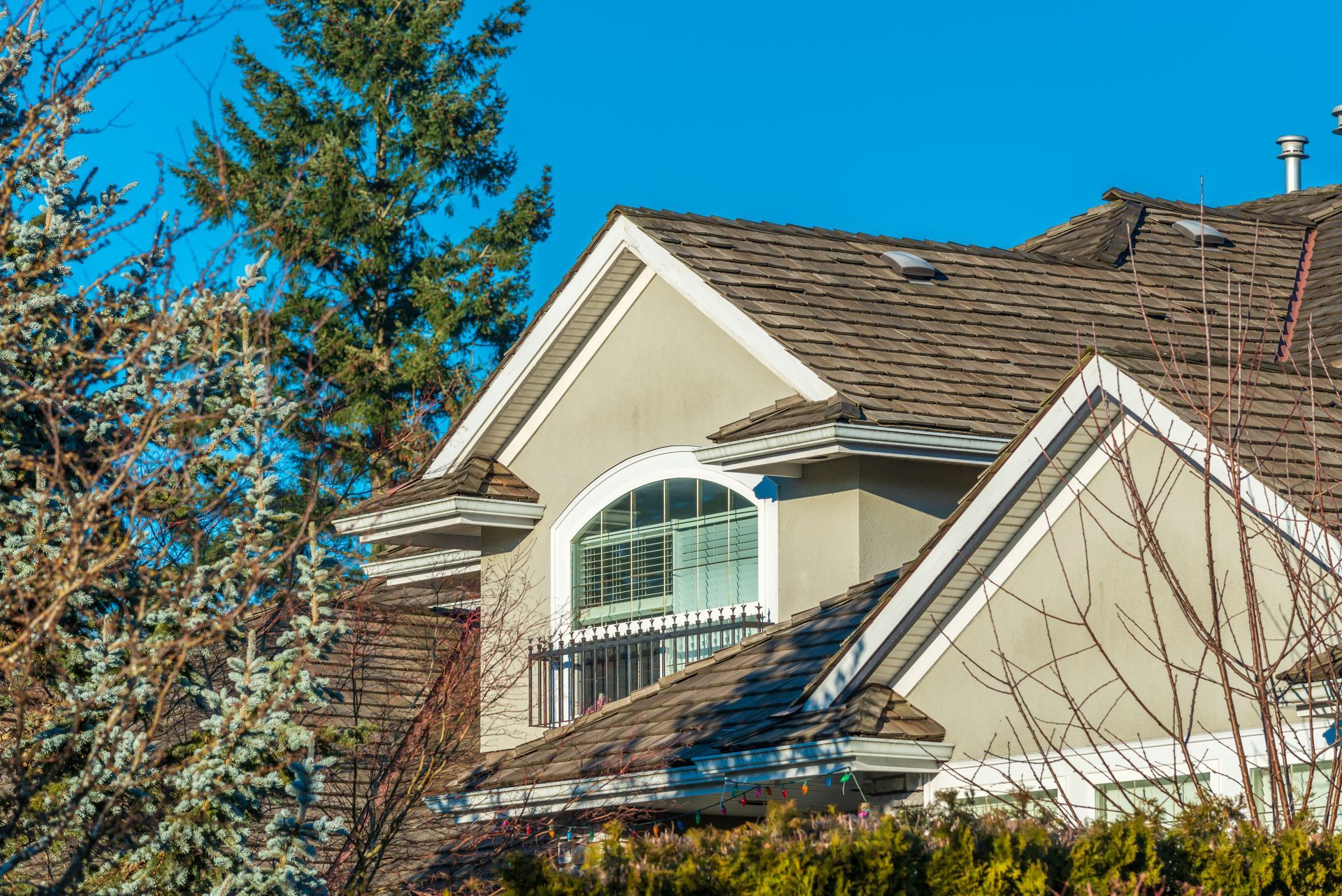 Residential home with a gray roof and light-colored siding under a clear blue sky.