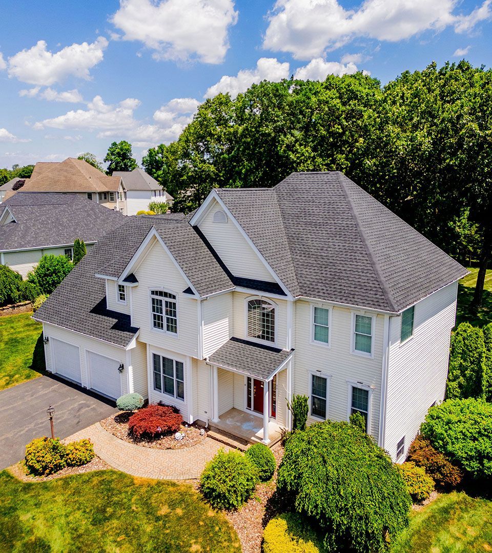 An aerial view of a large white house with a gray roof surrounded by trees.