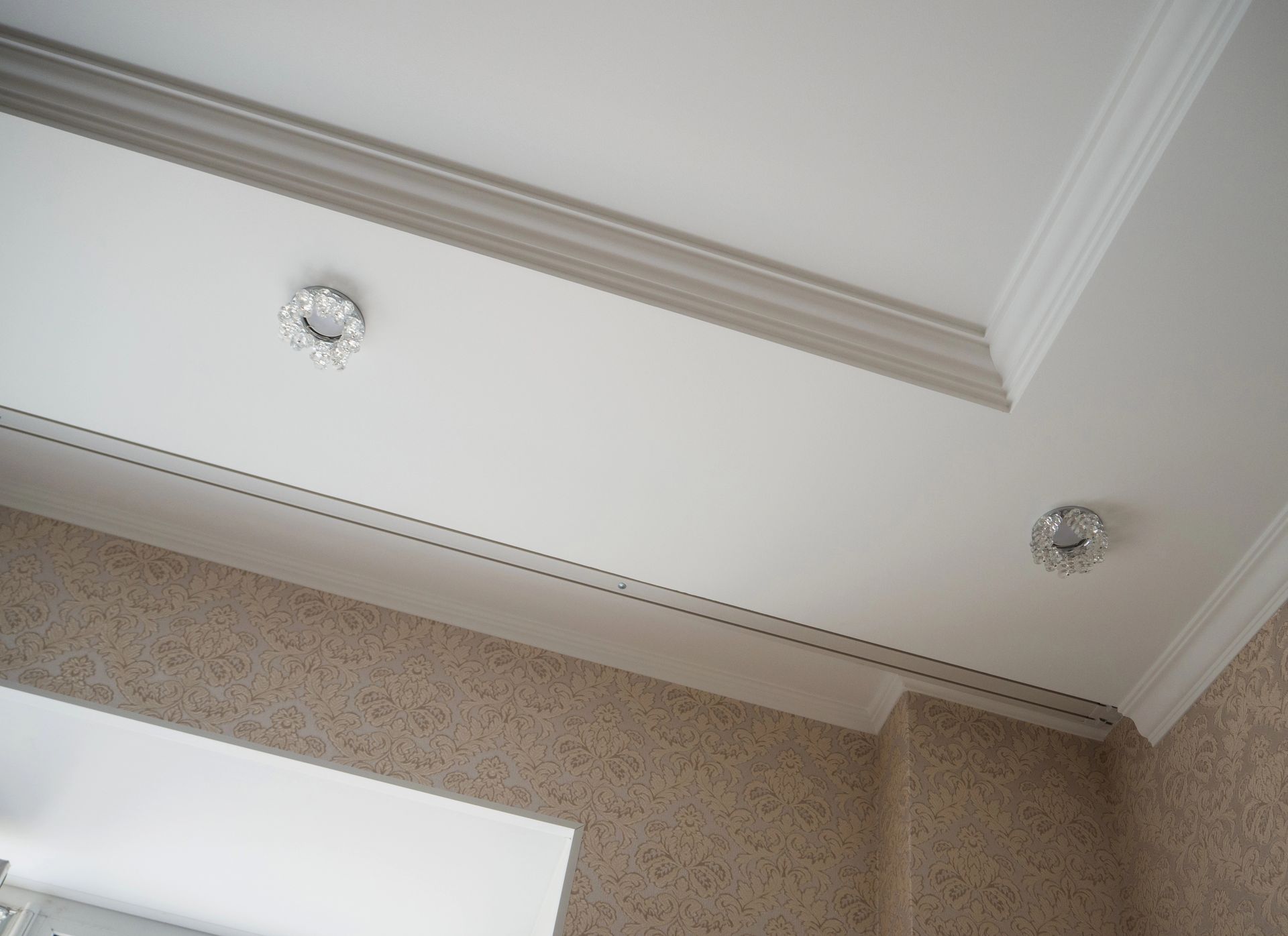 Soffitto bianco con modanature a corona, due luci da incasso e parete beige testurizzata.