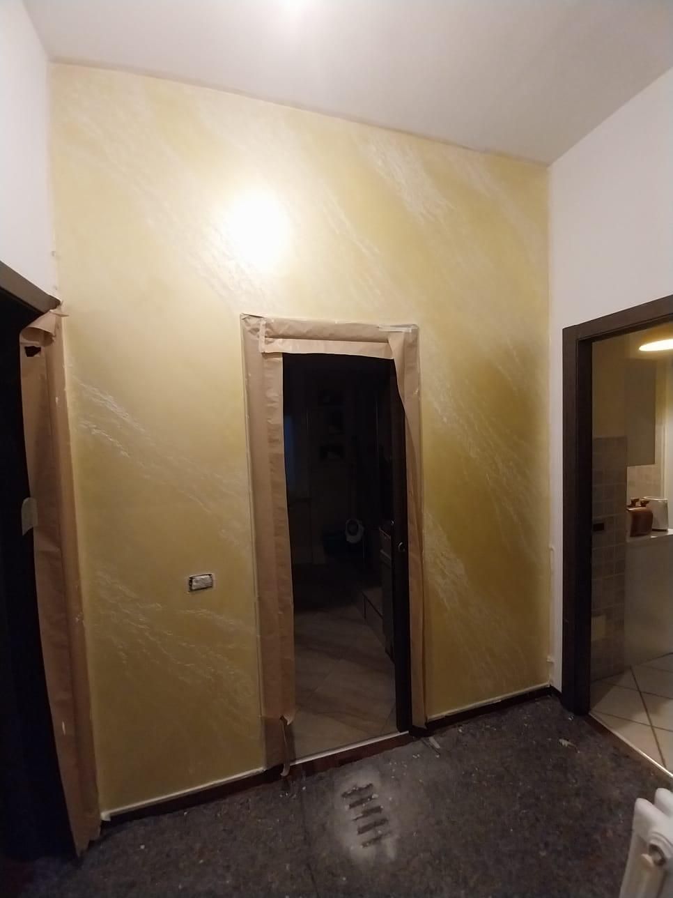 Corridoio con pareti dalla texture dorata, porte scure e una porta che conduce a una stanza buia.