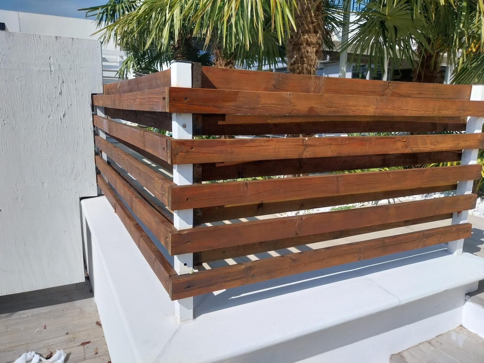 Fioriera in legno con assi orizzontali e supporti bianchi, per esterni.