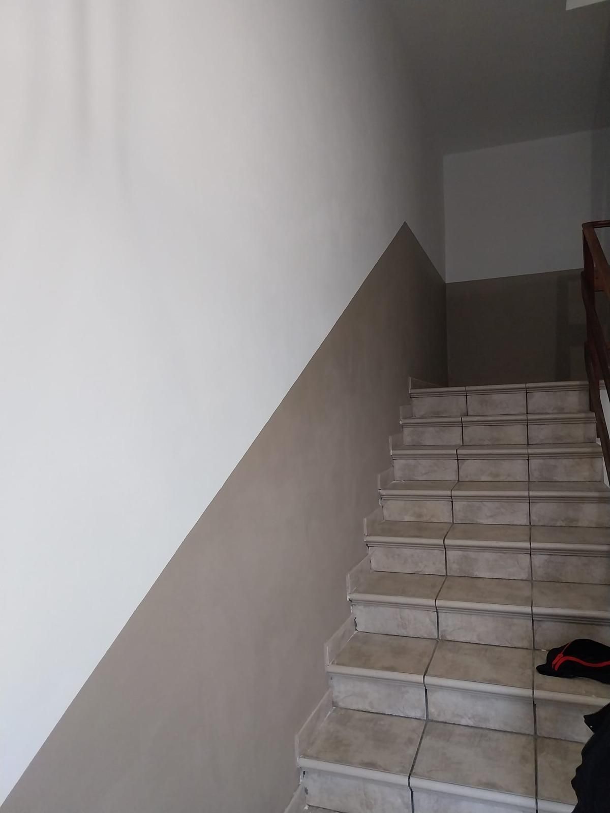 Scala con gradini in piastrelle chiare, che sale lungo una parete dipinta di bianco e una fascia grigio scuro.