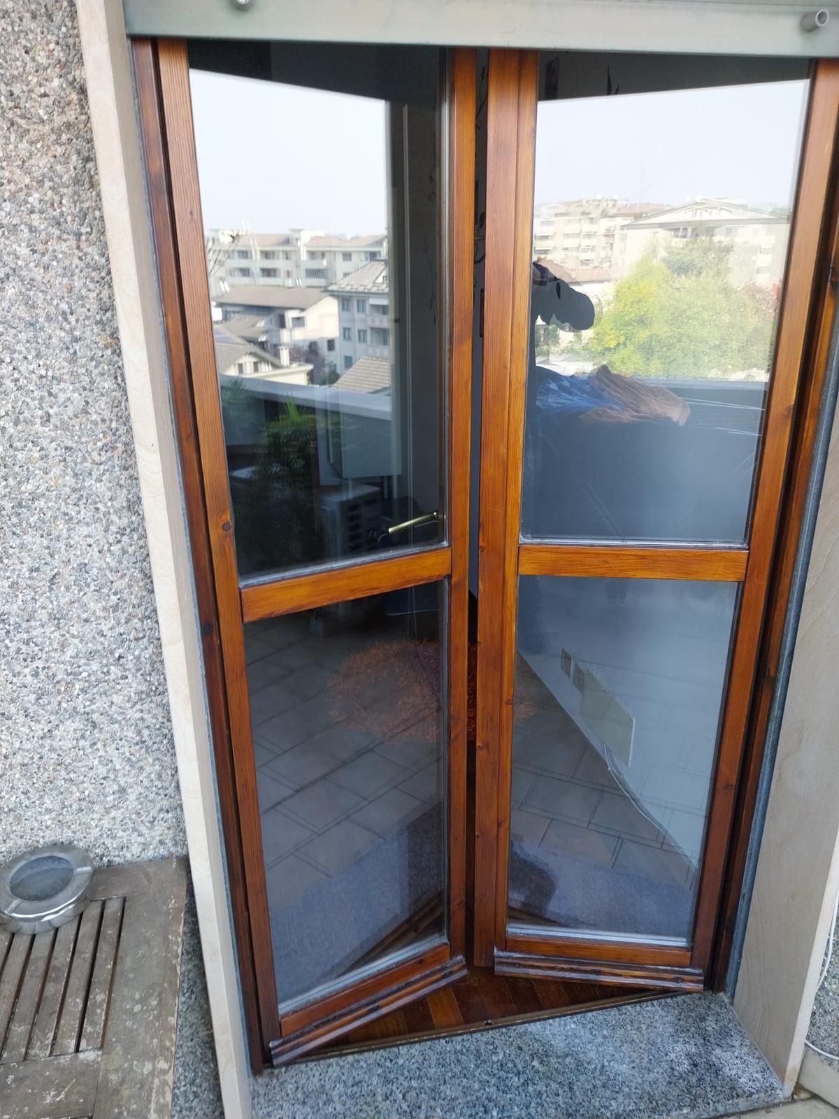 Le porte in vetro con cornice in legno si aprono su una vista urbana.