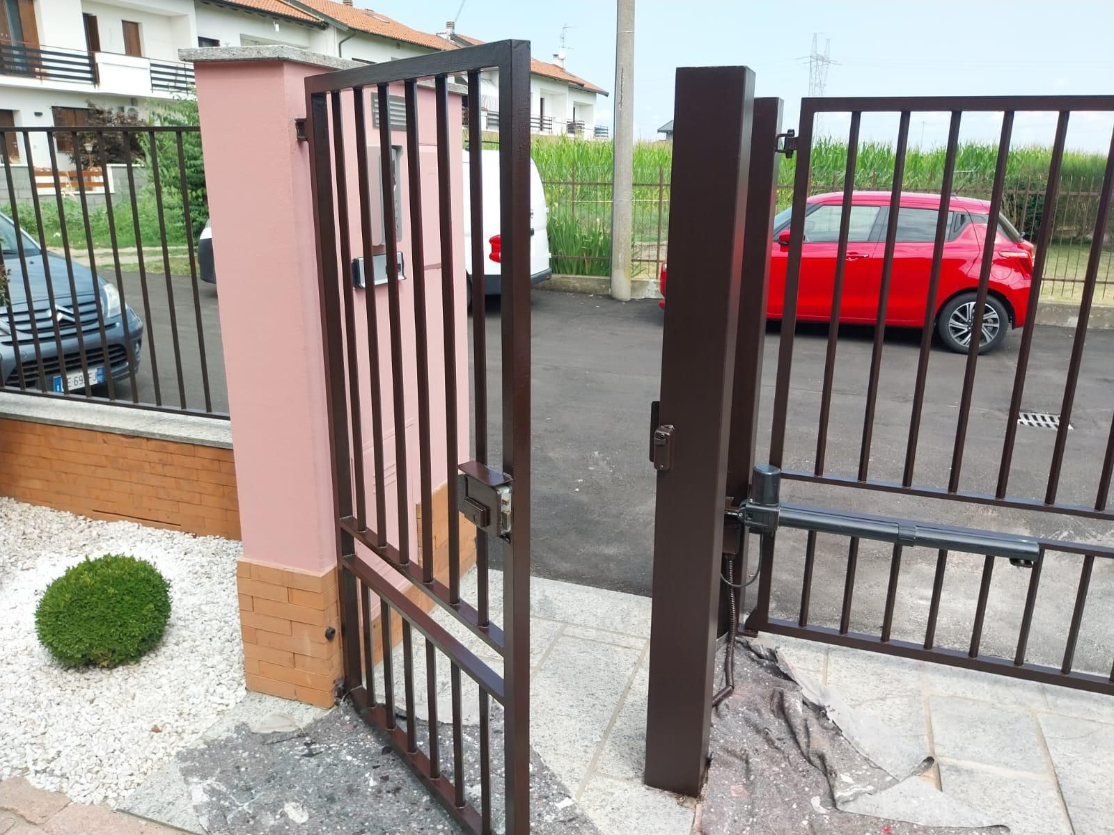 Cancello di metallo marrone, parzialmente aperto, su un vialetto. Un'auto rossa è visibile attraverso il cancello.
