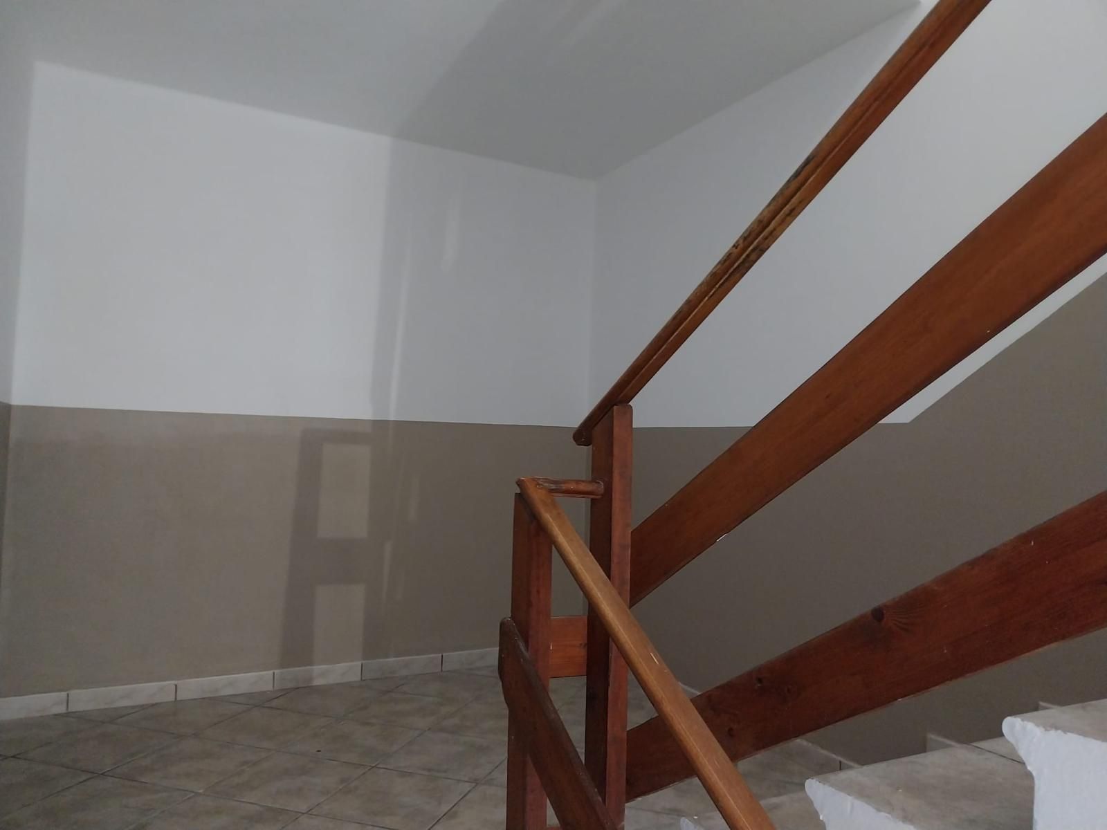 Scala con corrimano in legno e pareti dipinte di marrone e bianco. Pavimento piastrellato.