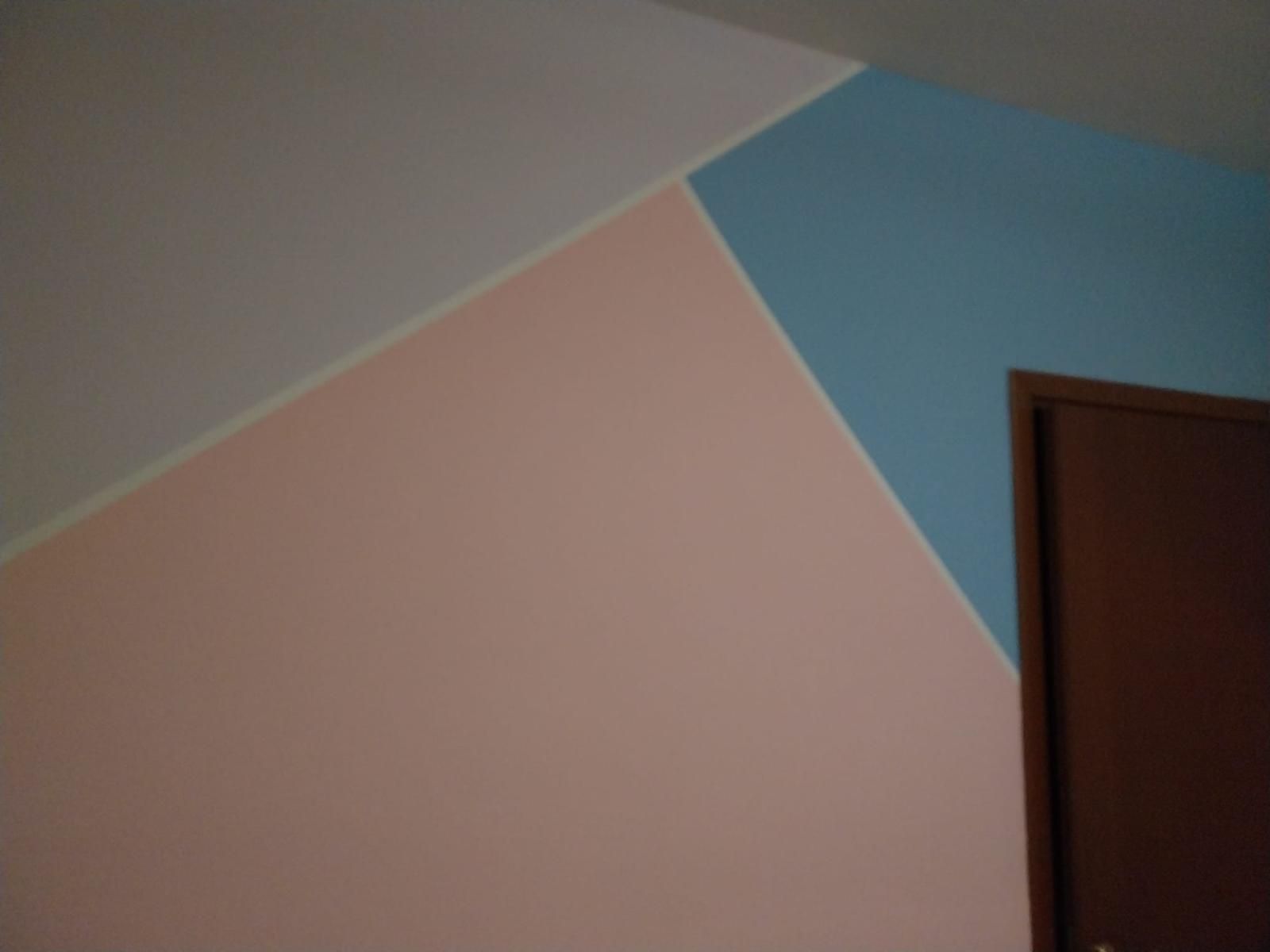 Parete con blocchi di colore geometrici, tinteggiata in rosa chiaro, blu e bianco. Porta marrone con cornice.