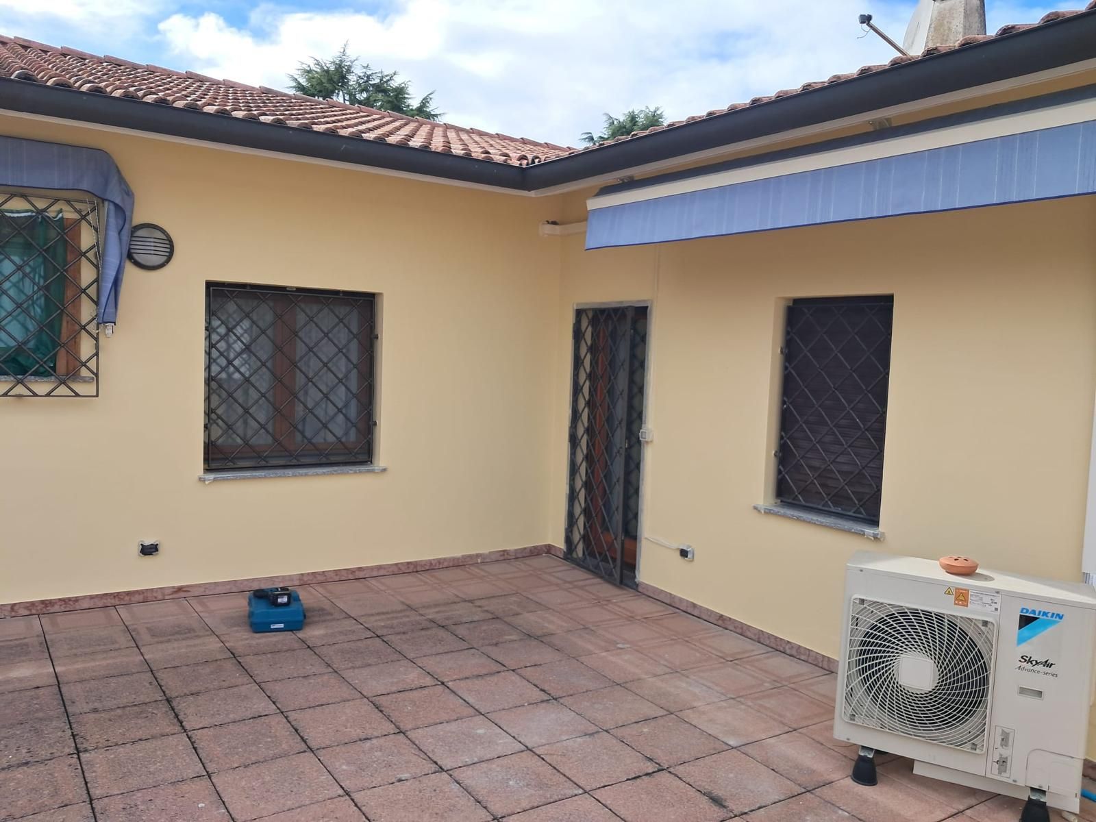 Patio con pareti gialle e piastrelle rosse, porta di sicurezza in metallo e aria condizionata.