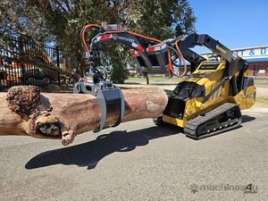 Yellow tracked loader carrying a large log on a road, with a logging attachment overhead