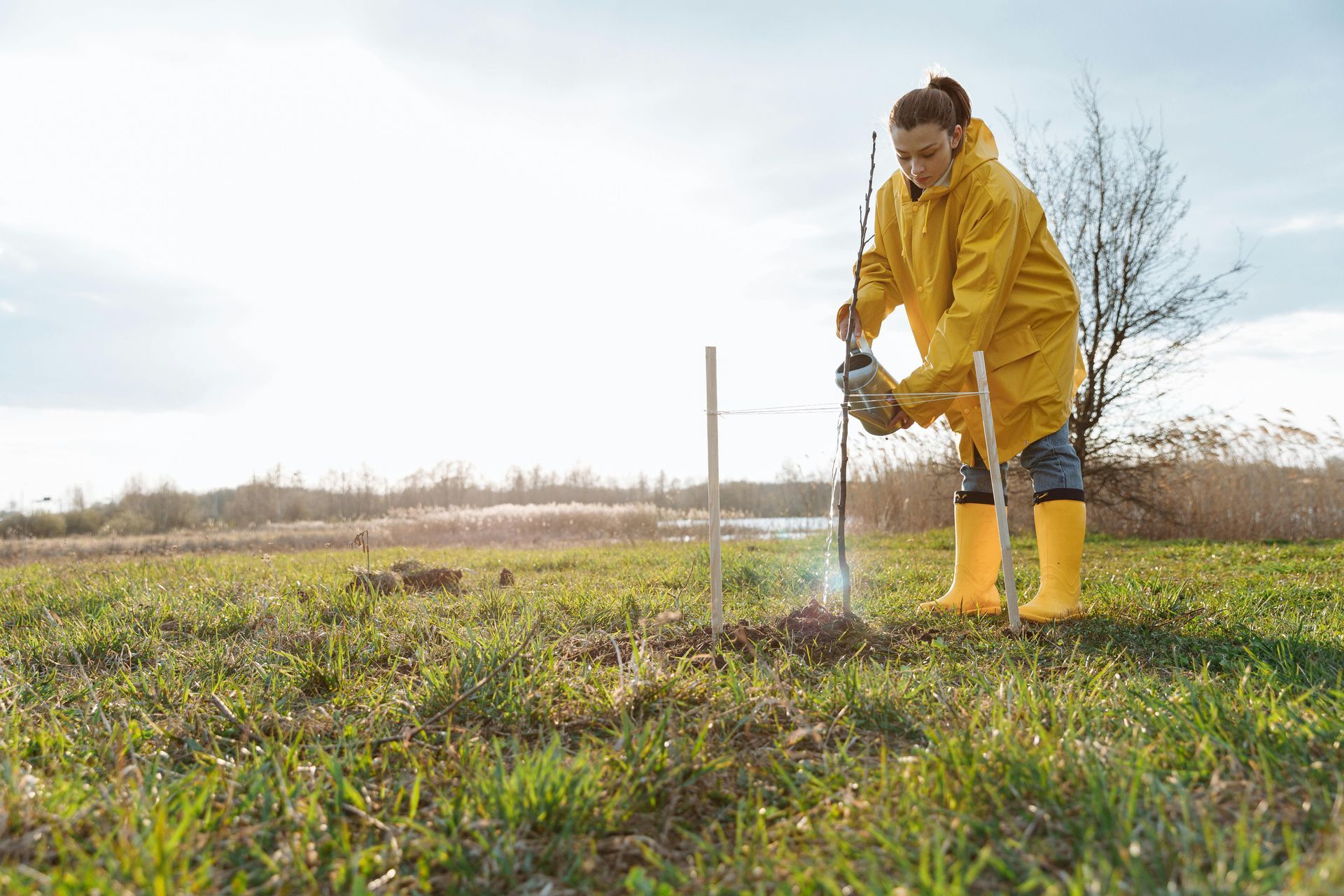 Person in yellow raincoat plants something outdoors with a shovel.