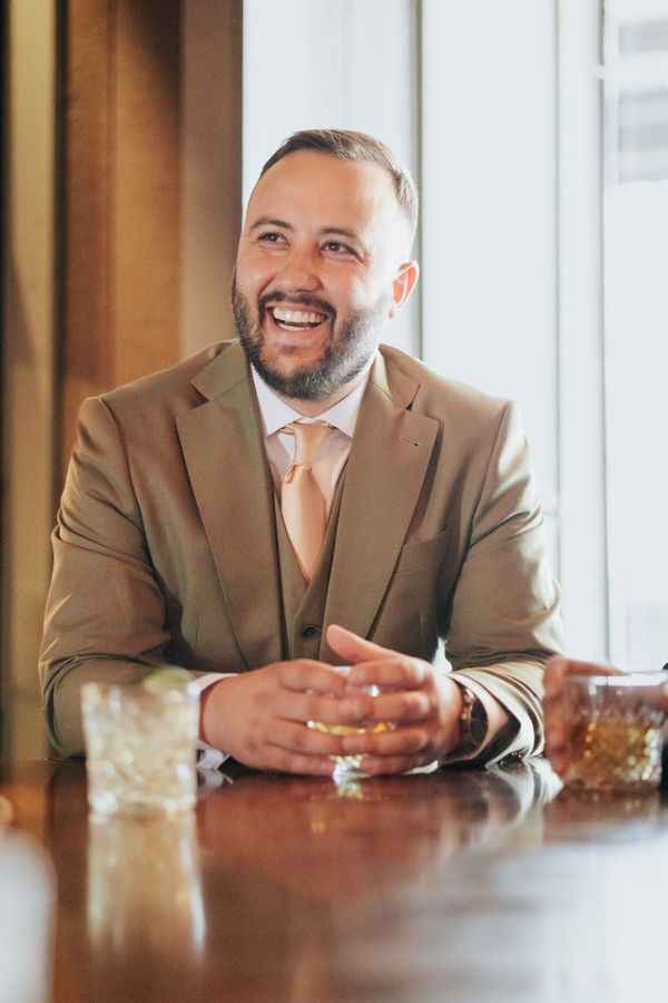 Smiling man in a tan suit seated at a table in a bright room