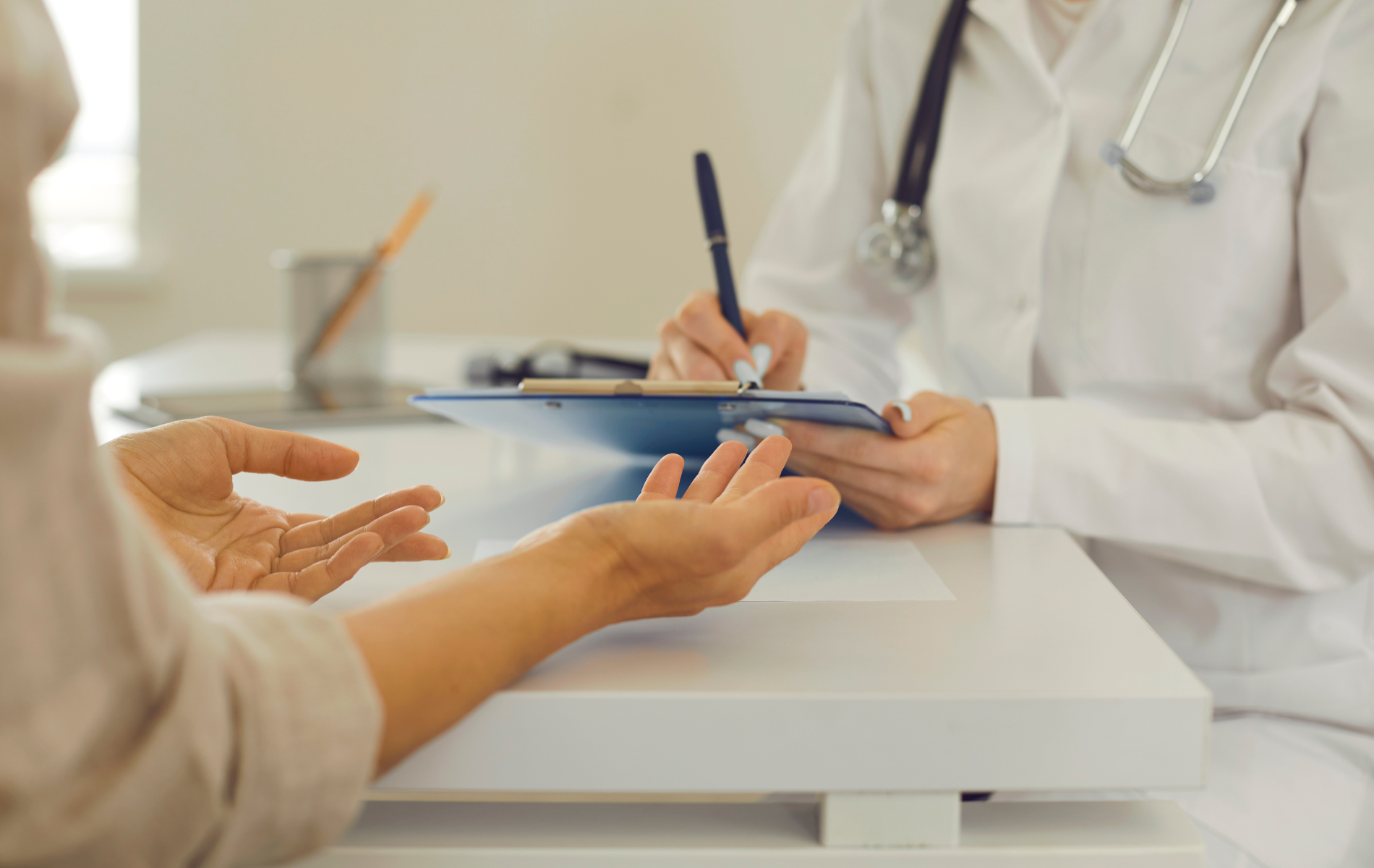 Patient speaking with a doctor across a desk in a bright clinic office.