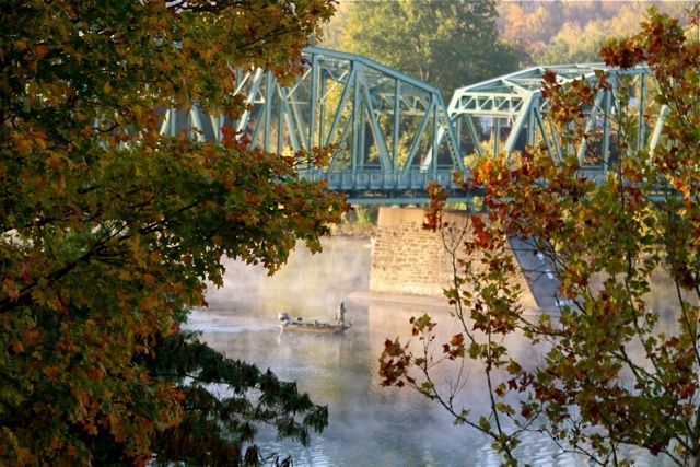 A bridge over a river with trees in the foreground and a boat in the background.