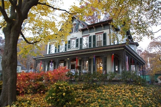A large house with a large porch is surrounded by trees and leaves.