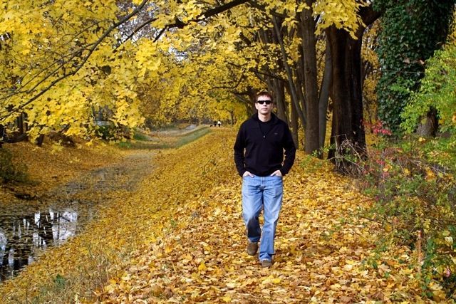 A man is walking down a path covered in leaves.