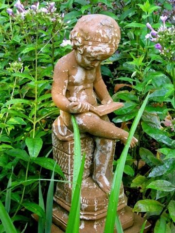A statue of a child reading a book in a garden