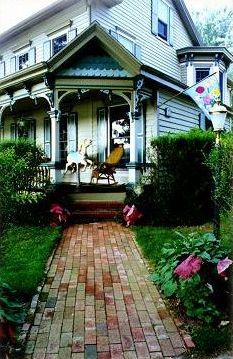 A brick walkway leading to a house with a merry go round on the porch.