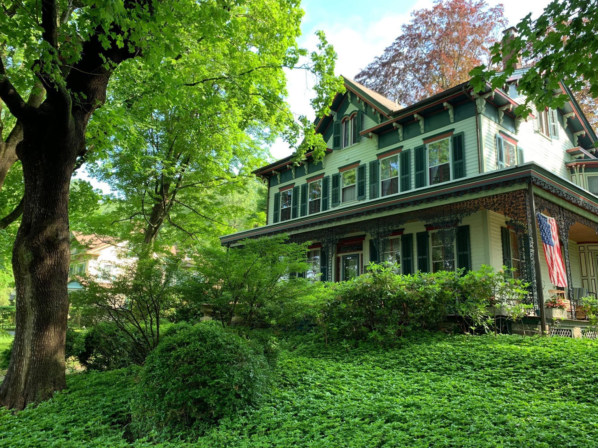 A large house with a large porch is surrounded by trees and bushes.