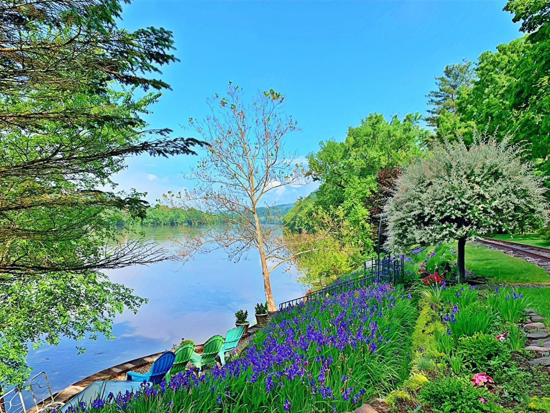 A painting of a river surrounded by trees and flowers.