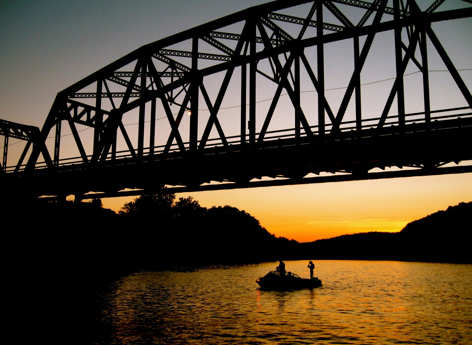 Two people in a boat under a bridge at sunset