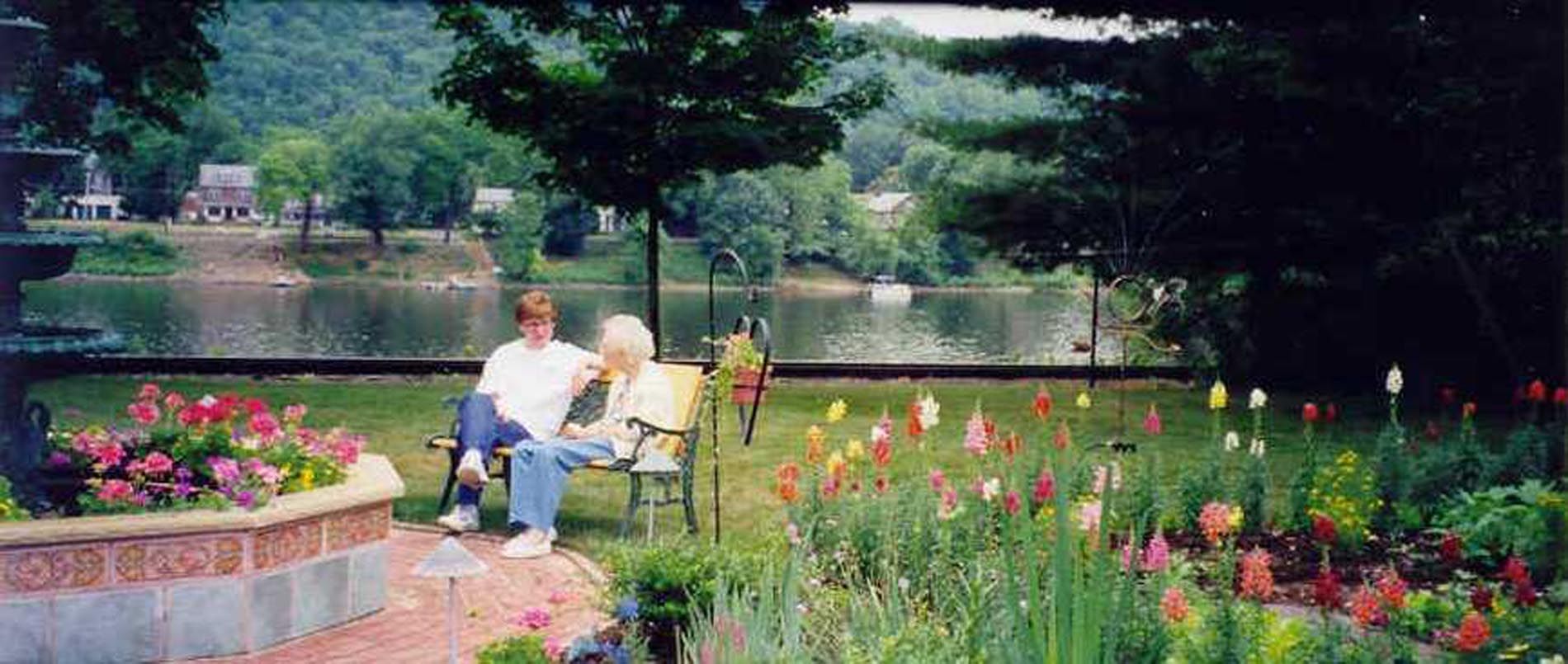 Two people are sitting on a bench in a park near a lake.