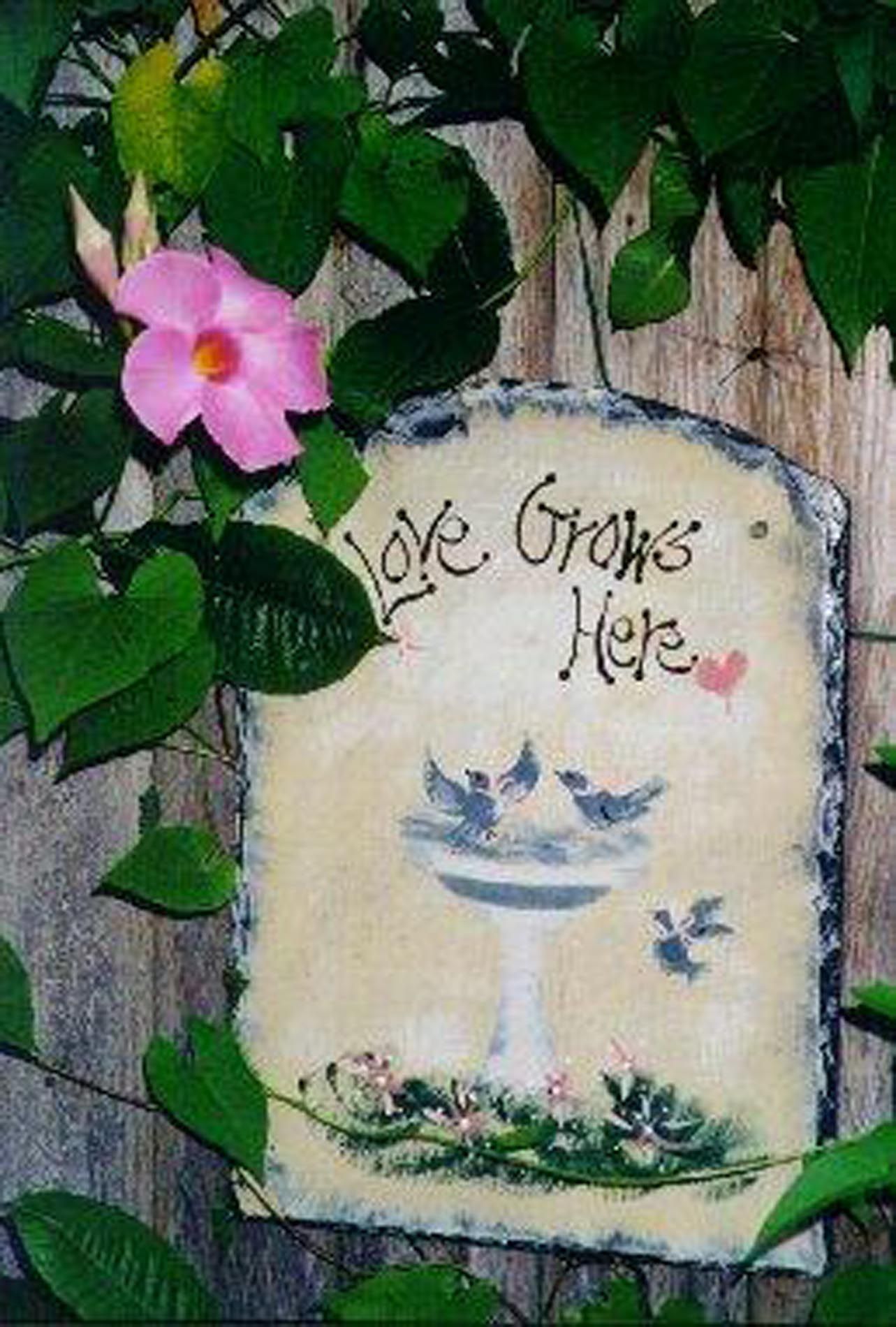A sign that says love grows here next to a pink flower