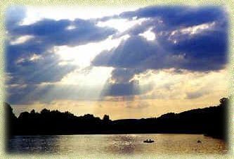 The sun is shining through the clouds over a lake