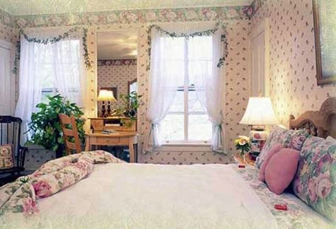 A bedroom with a bed , desk , lamps and a mirror.